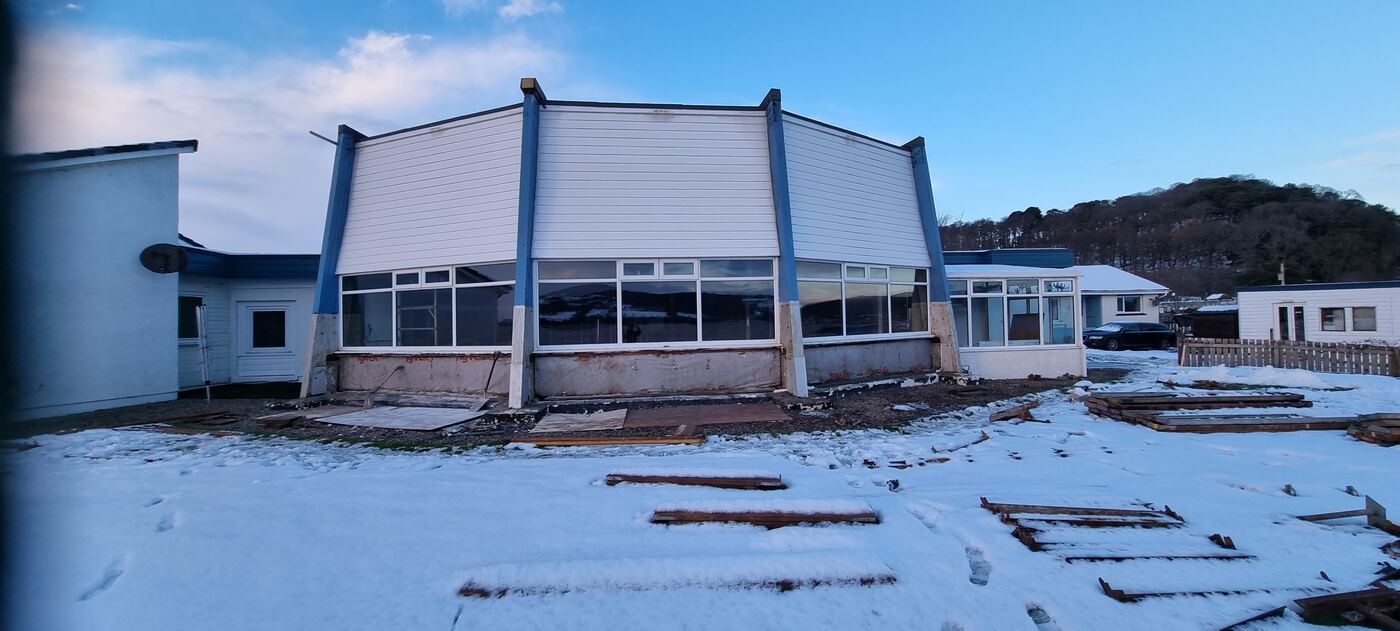The same building before renovation — old white weatherboard cladding, stripped back to bare framework in the snow