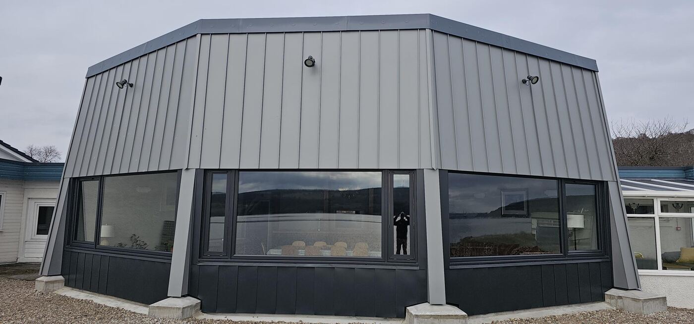 Completed building with dark grey standing-seam metal cladding and full-height glazing, overlooking the Cromarty Firth