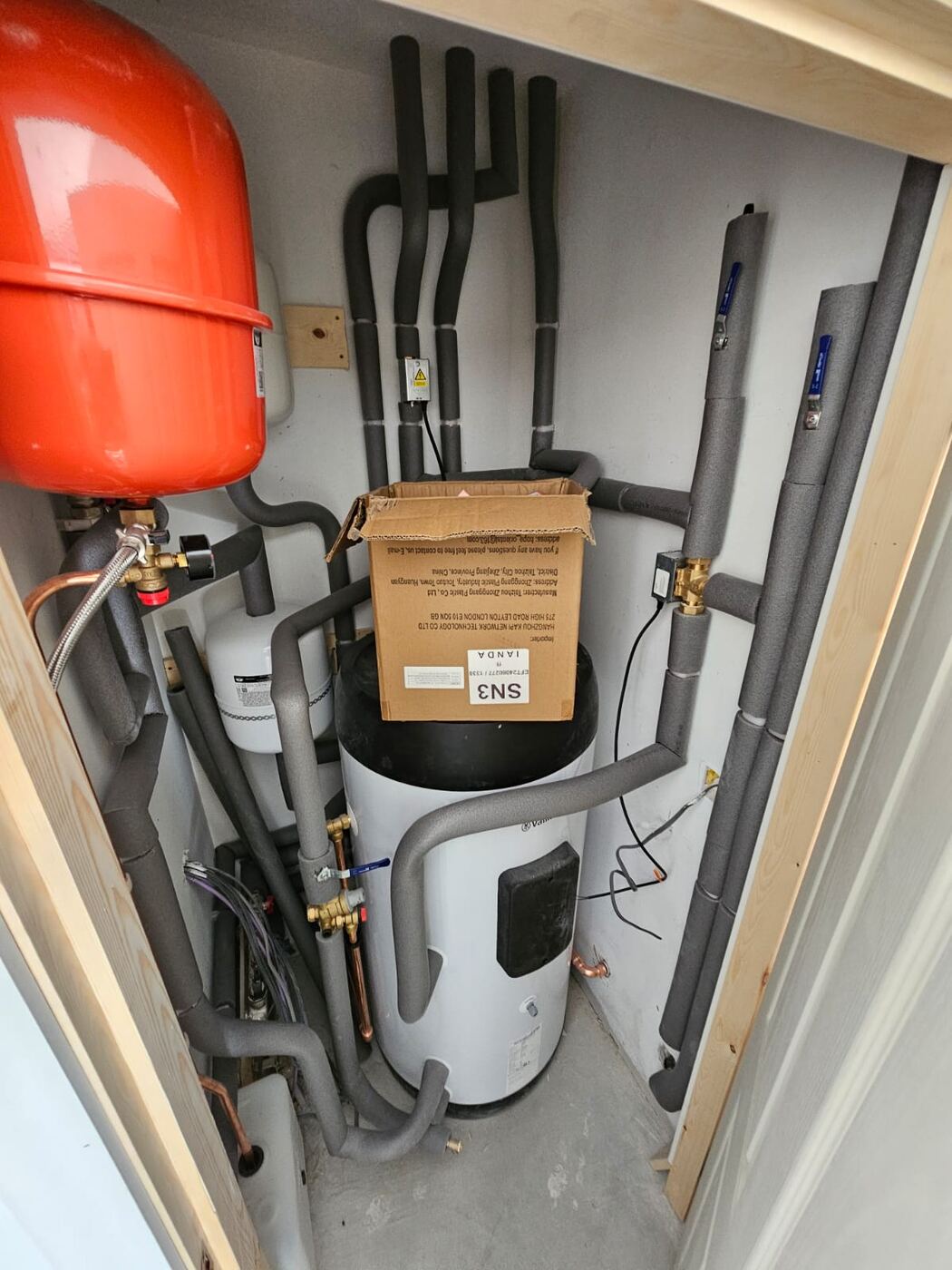 Plant cupboard with hot water cylinder, expansion vessel and insulated pipework feeding the heat pump system